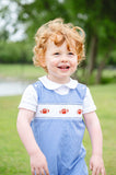 Little boy in a blue gingham jonjon with hand-smocked football panel, standing outdoors holding a football