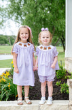 Two girls wearing matching light purple gingham smocked butterfly sets with hand-smocked orange monarch butterflies