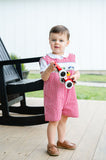Baby boy standing on porch wearing Smocked Race Car Jon Jon by Ruth and Ralph, red gingham, holding toy