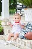 Baby girl wearing a white Pima cotton football bubble with game day print and red trim, with white bows and silver pom-poms