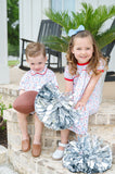 Little boy in a white and red game day romper with football print, standing on a brick porch holding a football