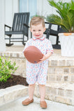 Toddler boy wearing a white Pima cotton football romper with game day print, red piping, and polo collar, holding a football