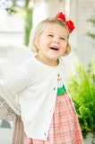 little girl wearing white cardigan with pom pom details.