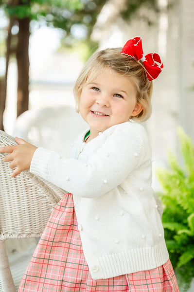 little girl wearing white cardigan with pom pom details.