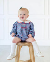 little girl sitting in blue floral bubble with smocking on chest.