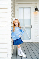 Girl standing wearing blue sweater with white bows and navy skirt.