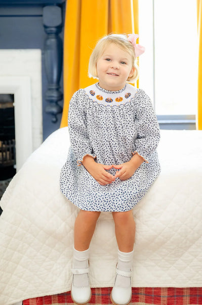 girl sitting wearing floral and smocked pumpkins dress