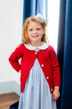 little girl wearing red cardigan with pom pom details.